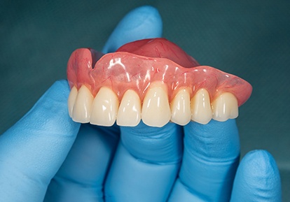 A closeup of a removable denture held by a gloved hand