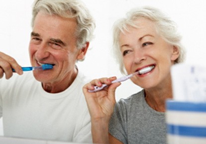 Senior couple smiling while brushing their teeth in bathroom