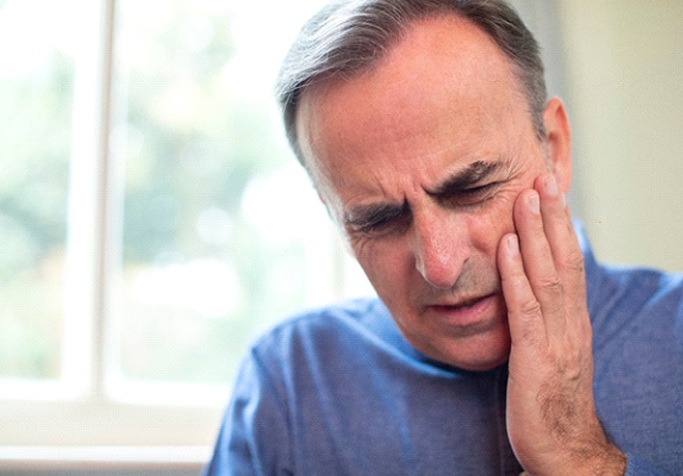 Man in blue shirt with hand on face due to dental pain