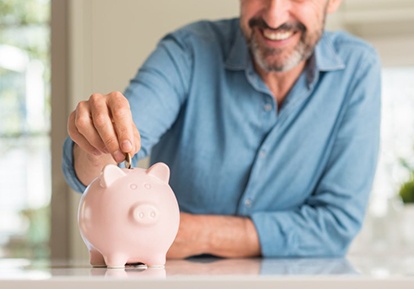 man putting coins into a pink piggy bank