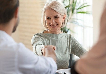 An older woman shaking hands with a dentist in Plainview to discuss dental implant eligibility