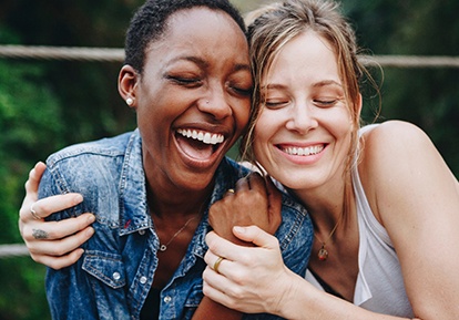 Two friends smiling while hugging outside