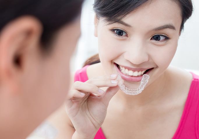 woman holding invisalign in front of smile and mirror