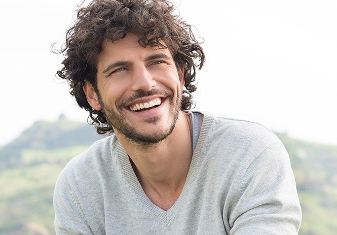man with curly hair smiling outside