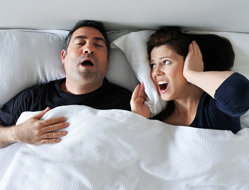 wife covering ears while husband snores
