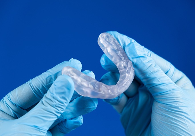 Gloved hands holding occlusal splint against blue background