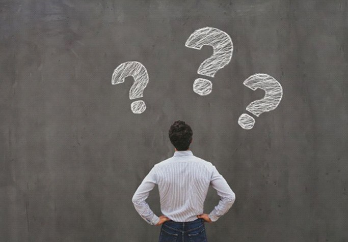 Man looking at chalkboard with question marks on it