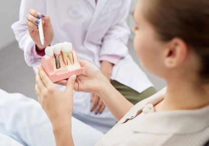 A female patient holds a mouth mold with a single tooth dental implant while a dentist explains whether she is an eligible candidate