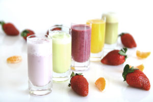 row of smoothies next to strawberries and orange slices