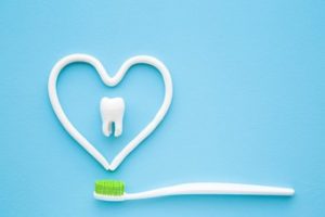 A heart shape drawn with toothpaste above a toothbrush with a tooth in the center against a blue background