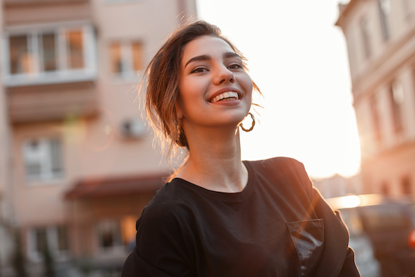 young white woman smiling in urban scene, sun and pink buildings behind her