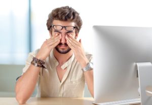 Man sitting at computer, dealing with eye pain